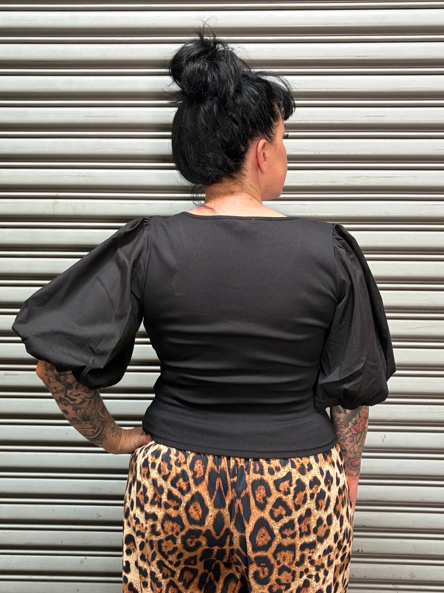A person wearing a black long-sleeve top and a leopard print skirt, photographed from above against a corrugated metal wall.