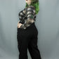 A model with green-tipped hair poses in a black and white plaid long-sleeve top and black wide-leg pants against a gray studio backdrop.