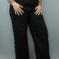Black wide-leg pants with silver grommet details down the outer side of each leg, worn by a model with a black belt and black top against a gray studio background.