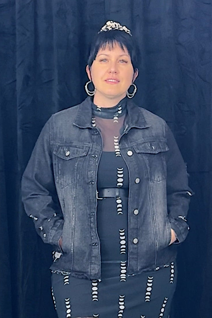 Person wearing a denim jacket and patterned dress against a dark curtain