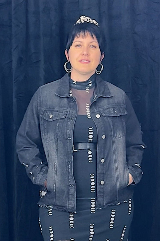 Person wearing a denim jacket and patterned dress against a dark curtain