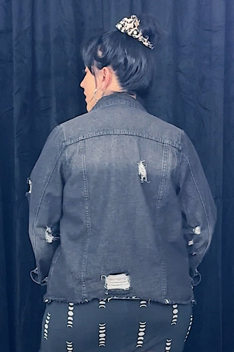 Person wearing a dark denim jacket and black skirt with sheer panels against a black background