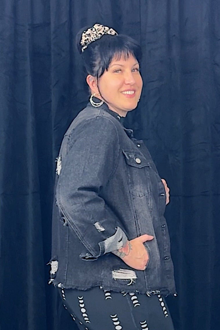 Person wearing a denim jacket and patterned skirt against a dark curtain background