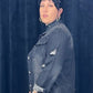 Person wearing a denim jacket and black skirt against a dark blue curtain.