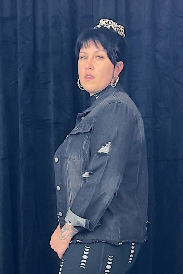 Person wearing a denim jacket and black skirt against a dark blue curtain.