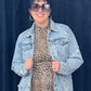 Person wearing a leopard print dress with a denim jacket against a black background