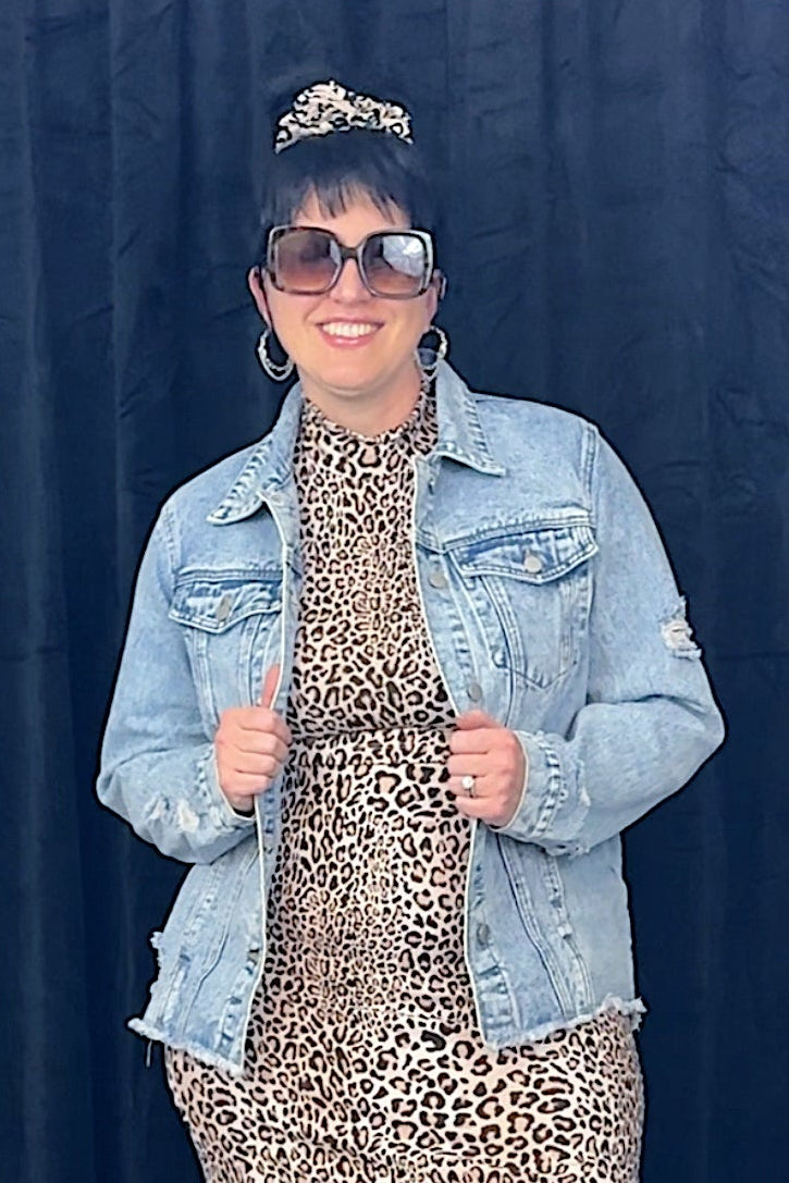 Person wearing a leopard print dress with a denim jacket against a black background