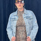 Person wearing a leopard print dress and denim jacket against a dark blue curtain.