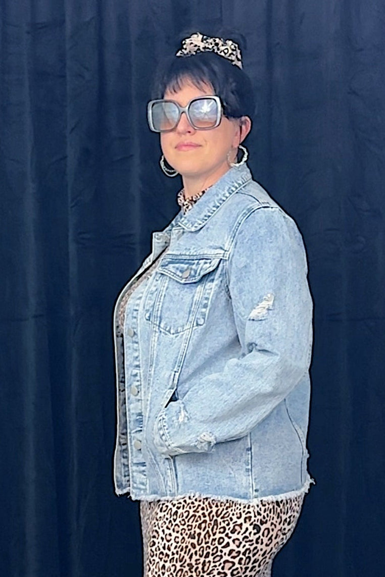Person wearing a denim jacket and leopard print skirt against a dark blue curtain.