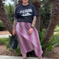 Person wearing a black t-shirt and pink skirt standing in front of palm trees.