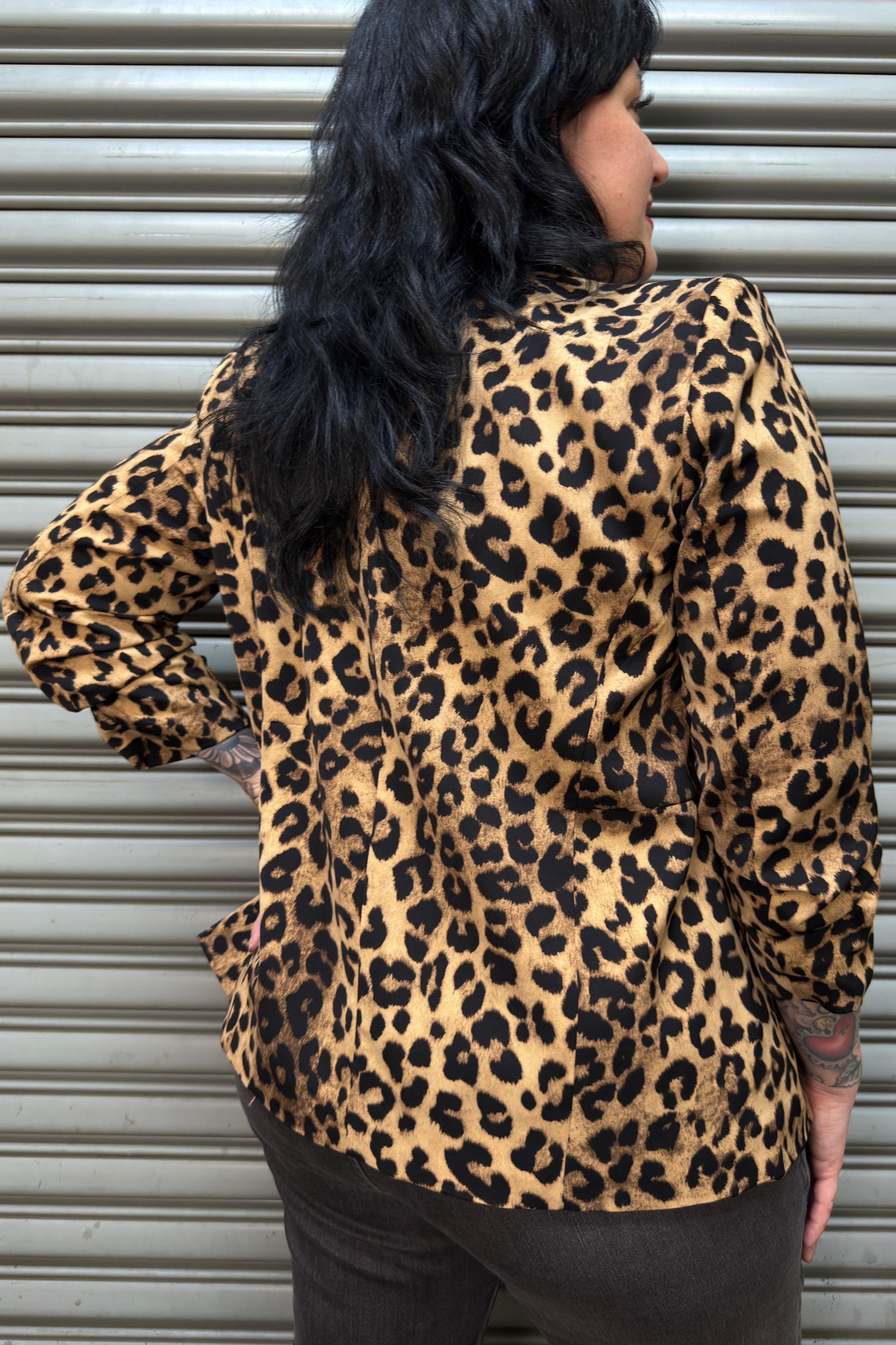 Person wearing a leopard print jacket standing in front of a metallic shutter.
