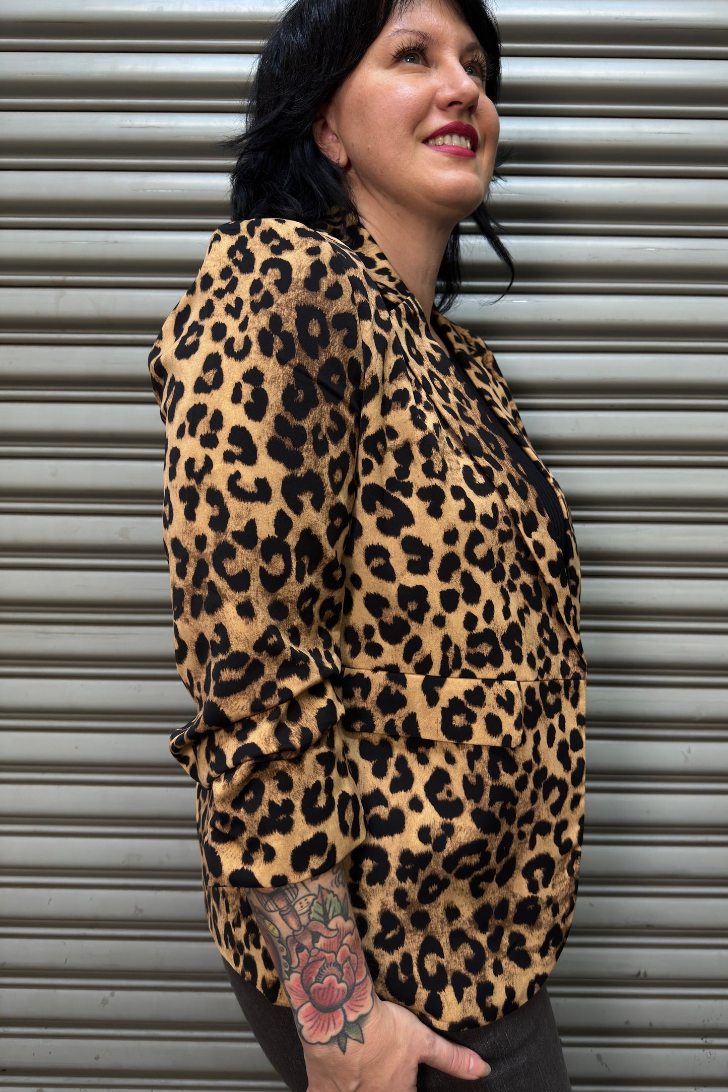 Person wearing a leopard print jacket standing against a metallic shutter.