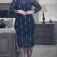 Woman wearing a black dress with white patterns in a bedroom setting