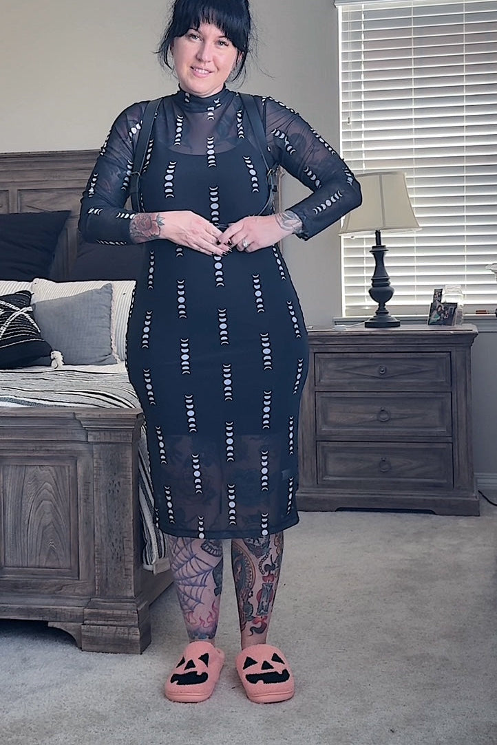 Woman wearing a black dress with white patterns in a bedroom setting