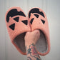 Pink slippers with black paw prints held by a hand with tattoos against a white background