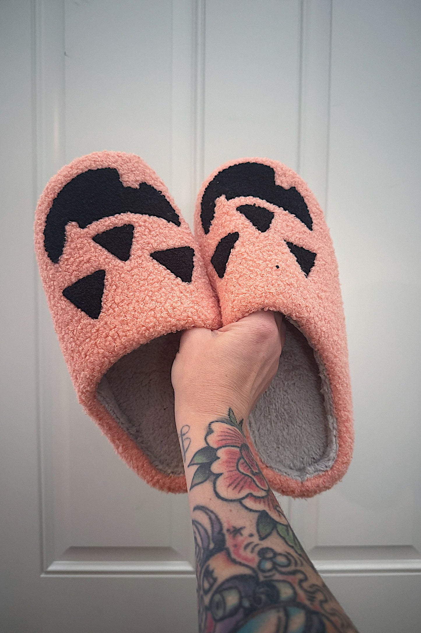 Pink slippers with black paw prints held by a hand with tattoos against a white background