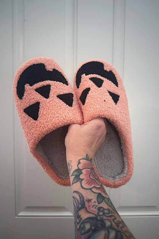 Pink slippers with black paw prints held by a hand with tattoos against a white background