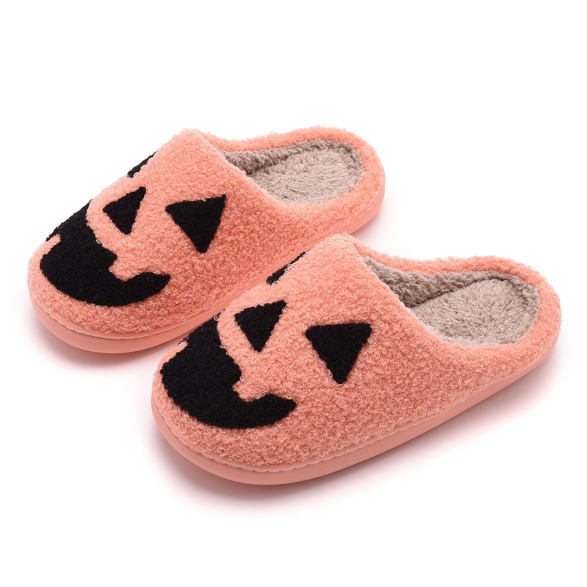 Pair of pink slippers with black jack-o'-lantern faces on a white background