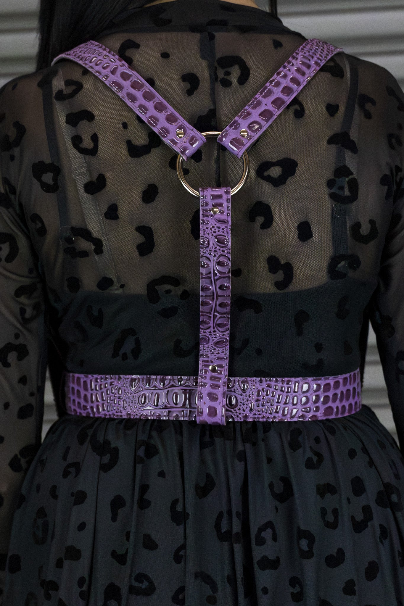 Purple harness with a gold ring on a black dress with leopard print details.
