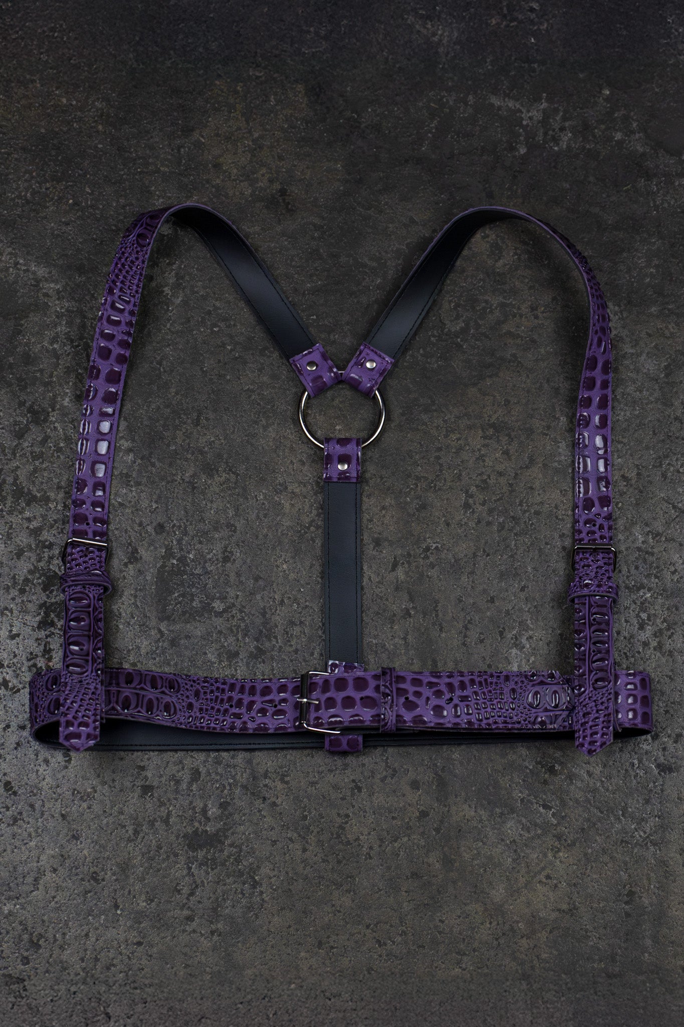 Purple leather harness with crocodile texture on a dark gray background