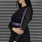 Woman wearing a black dress with a purple harness against a metallic background