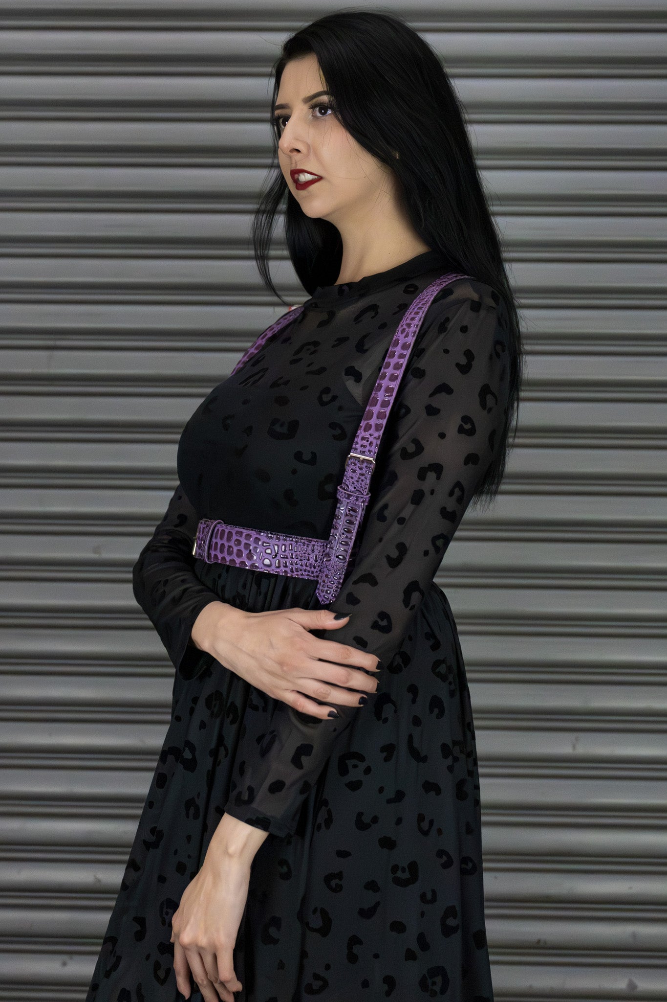Woman wearing a black dress with a purple harness against a metallic background