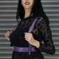 Woman wearing a black sheer top with leopard print and a purple harness against a metallic background