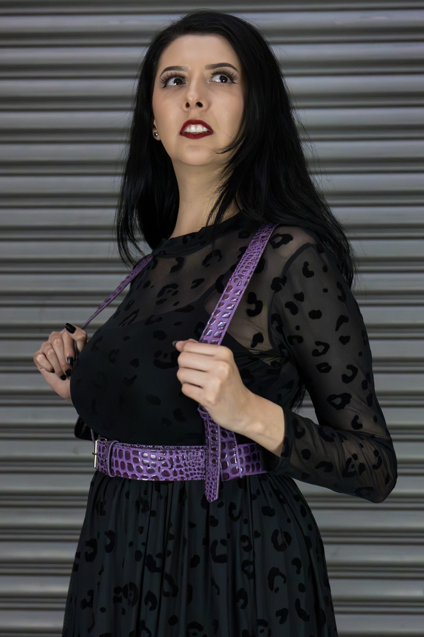 Woman wearing a black sheer top with leopard print and a purple harness against a metallic background