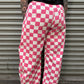 Person wearing pink and white checkered pants standing in front of a metal shutter.