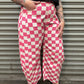 Person wearing pink and white checkered pants standing against a metal shutter.