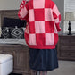 Person wearing a red and pink checkered sweater in a room with furniture and decor.