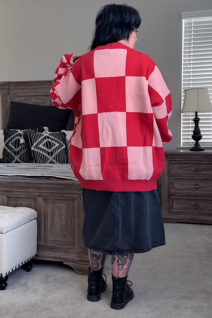 Person wearing a red and pink checkered sweater in a room with furniture and decor.
