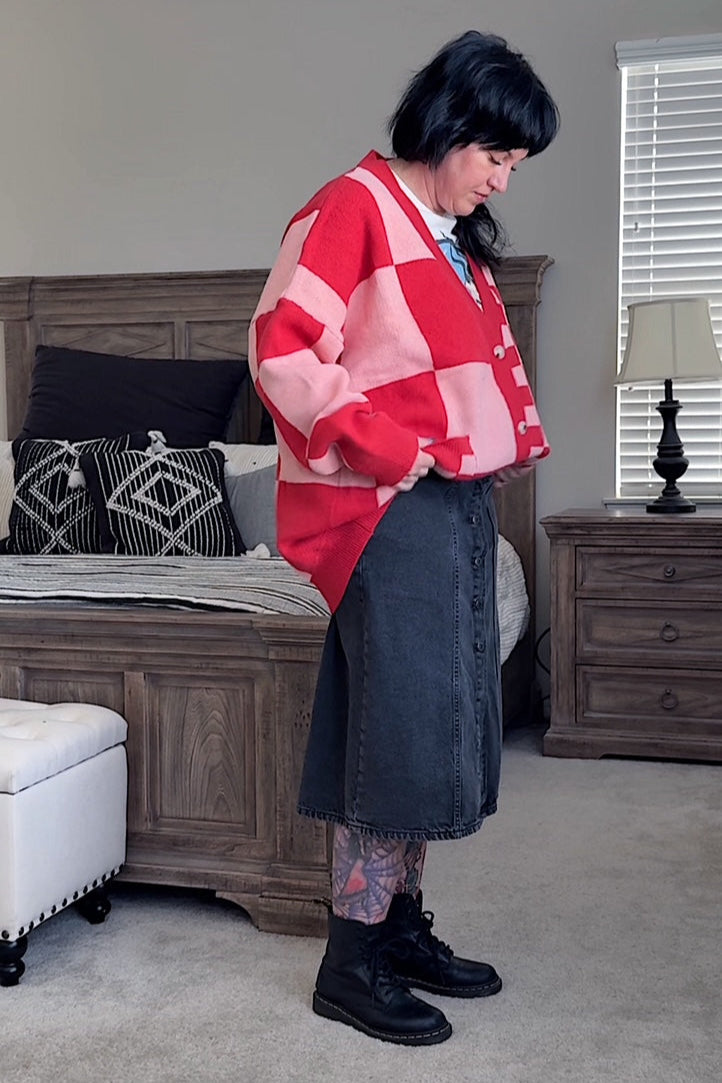 Person wearing a red and pink patterned cardigan in a bedroom setting