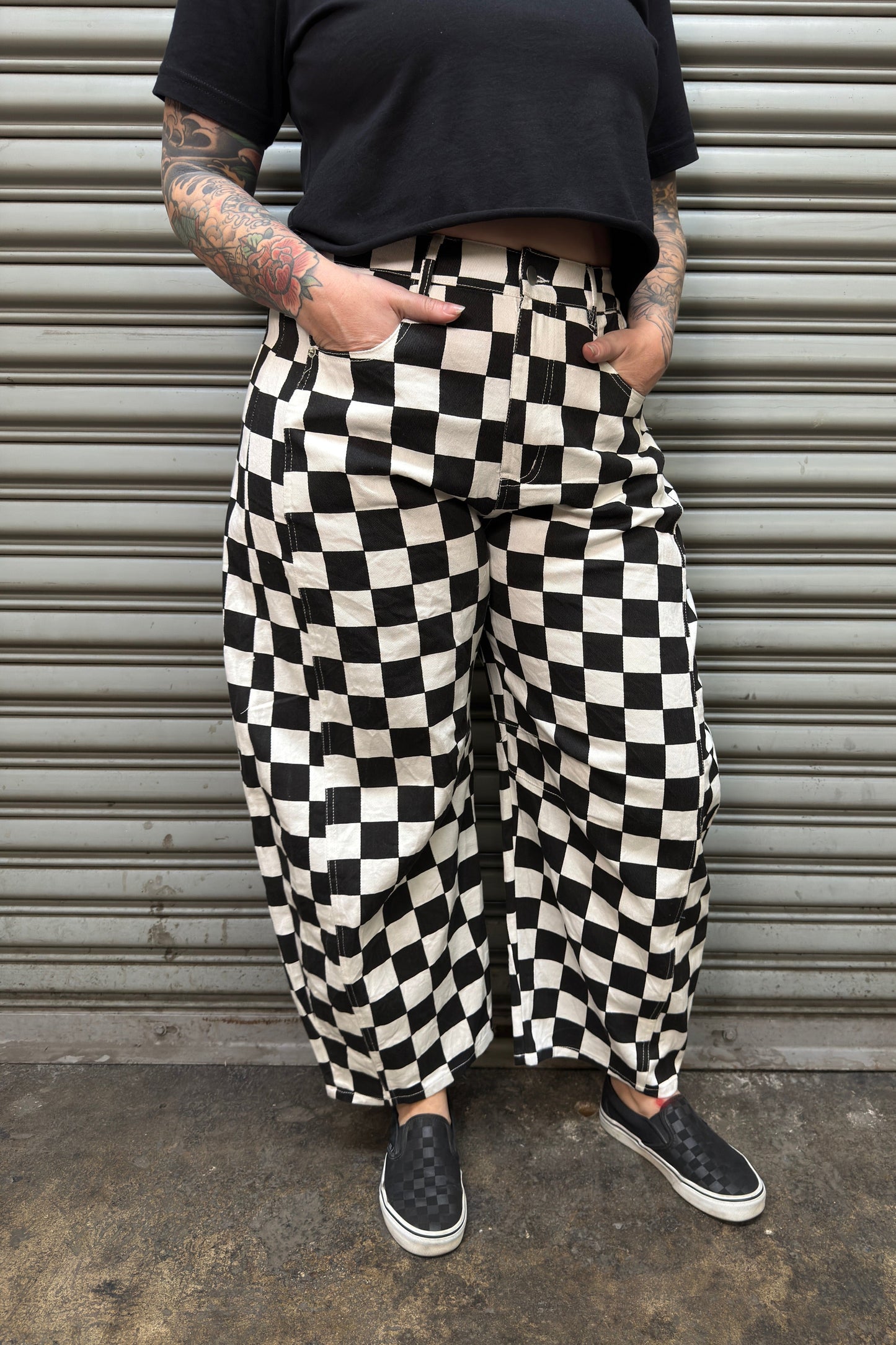 Person wearing black and white checkered pants standing against a metallic shutter.