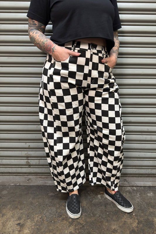 Person wearing black and white checkered pants standing against a metallic shutter.