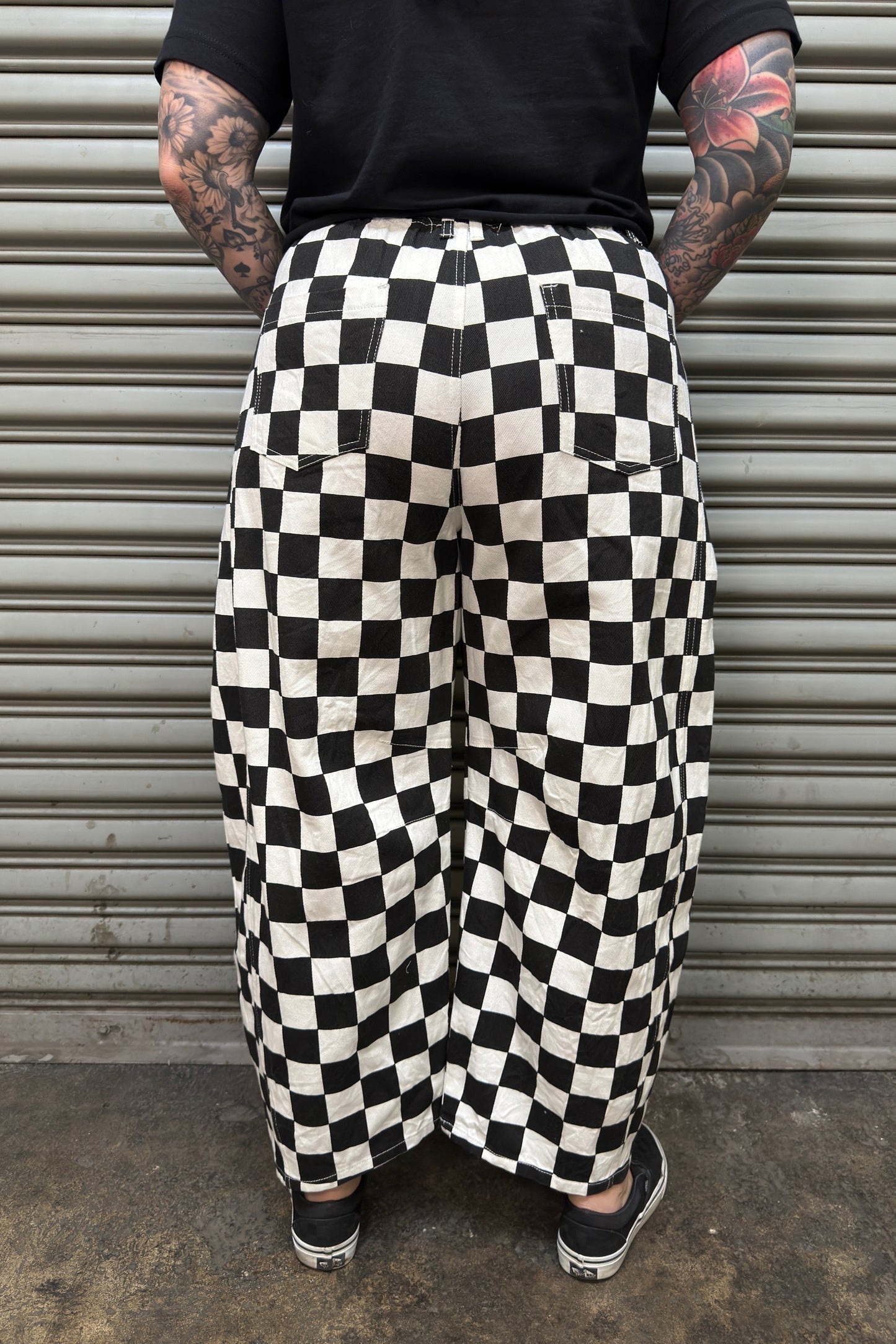 Person wearing black and white checkered pants standing in front of a metal shutter.