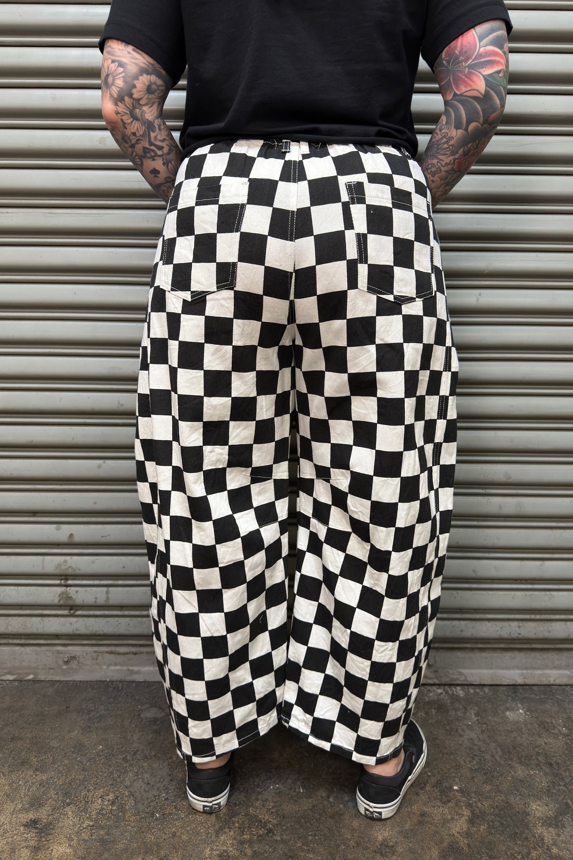 Person wearing black and white checkered pants standing in front of a metal shutter.