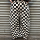 Person wearing black and white checkered pants standing against a metallic shutter.
