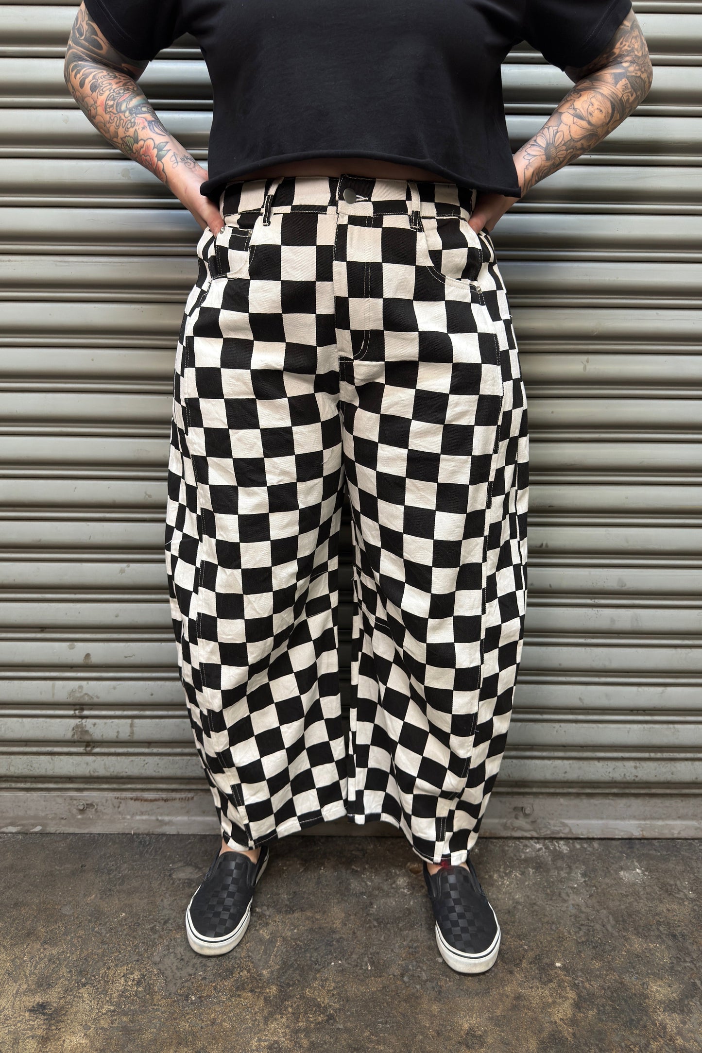 Person wearing black and white checkered pants standing against a metallic shutter.
