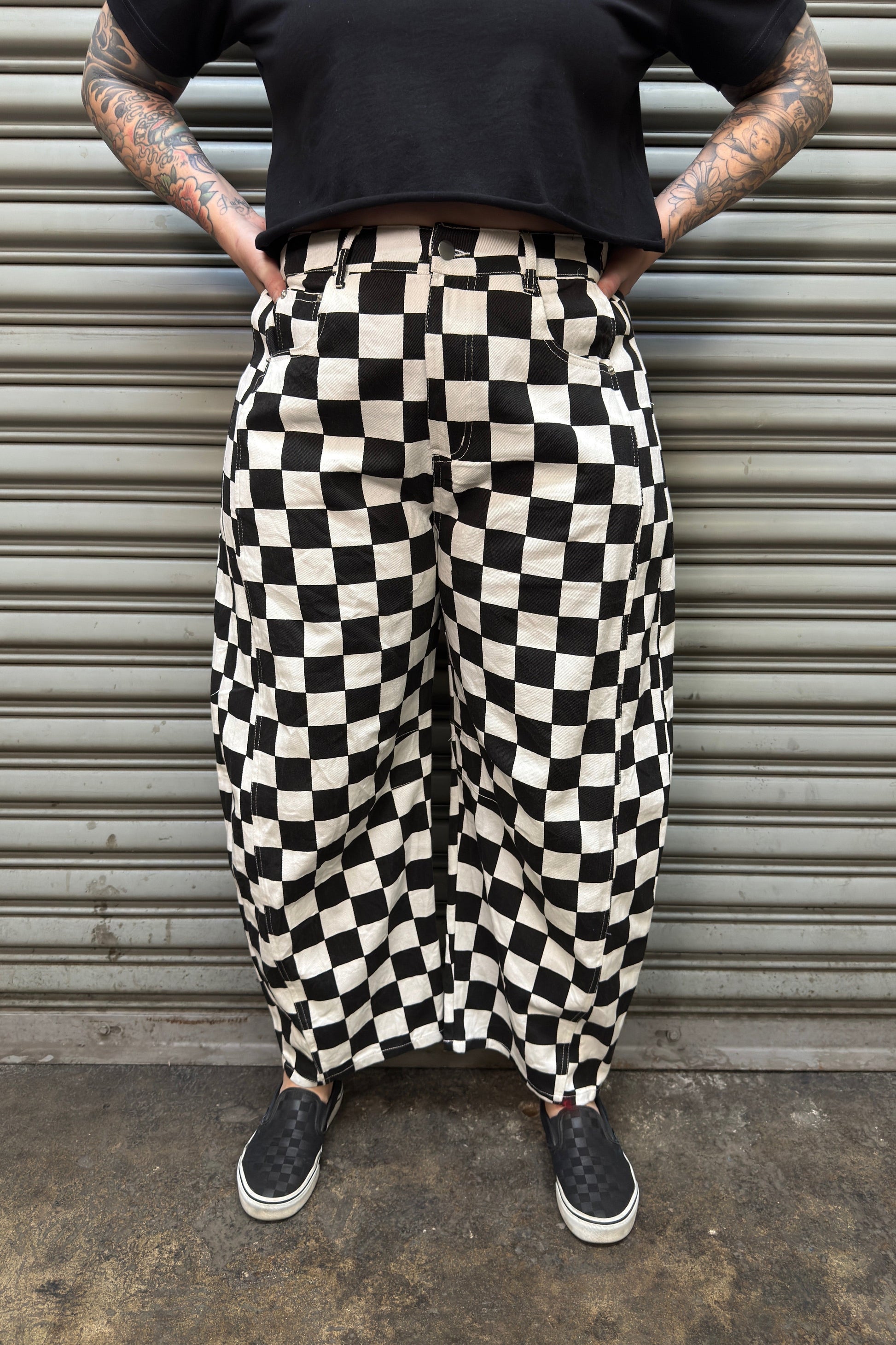 Person wearing black and white checkered pants standing against a metallic shutter.