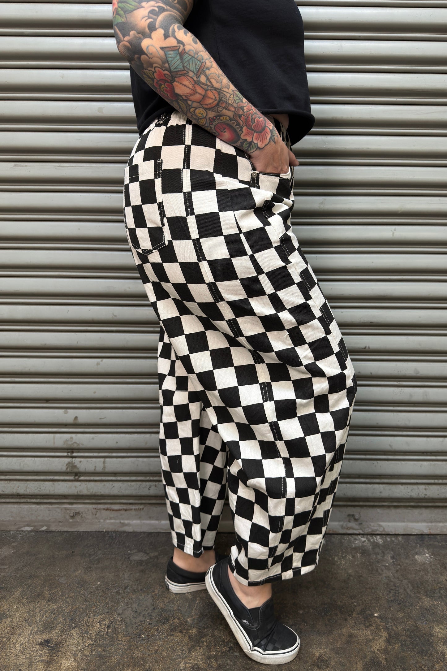 Person wearing black and white checkered pants standing in front of a metal shutter.