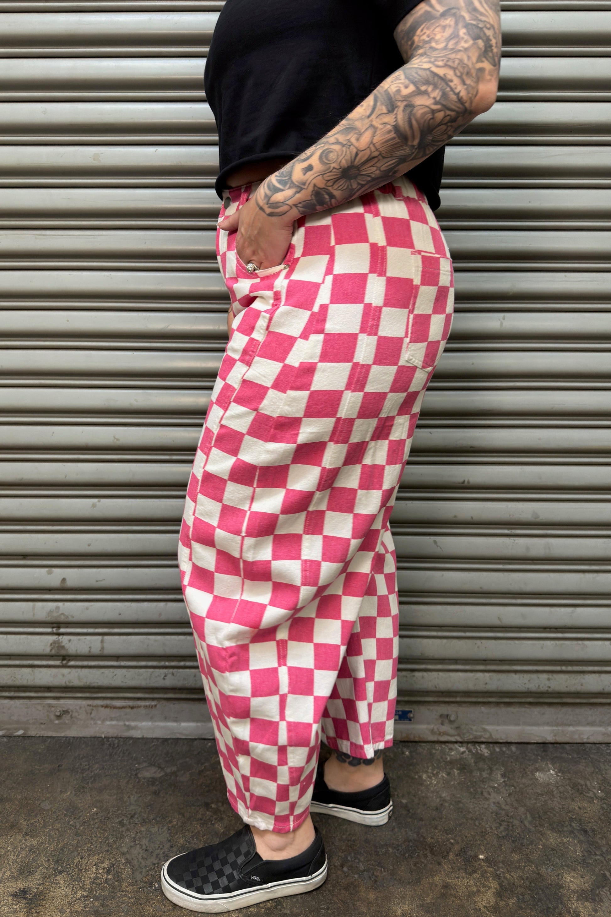 Person wearing pink and white checkered pants standing in front of a metal shutter.