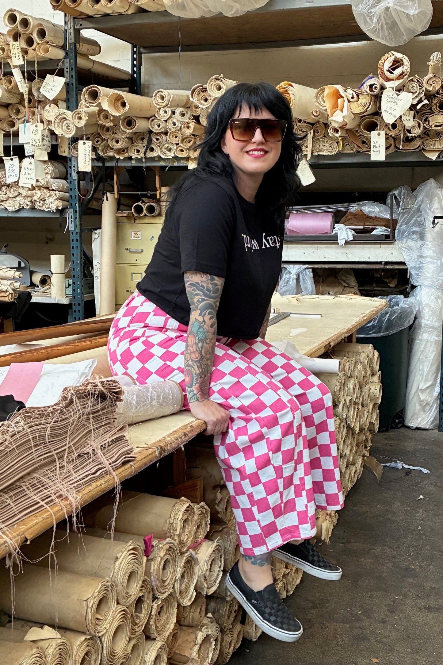 Person in a storage room with shelves filled with rolls of paper or fabric.