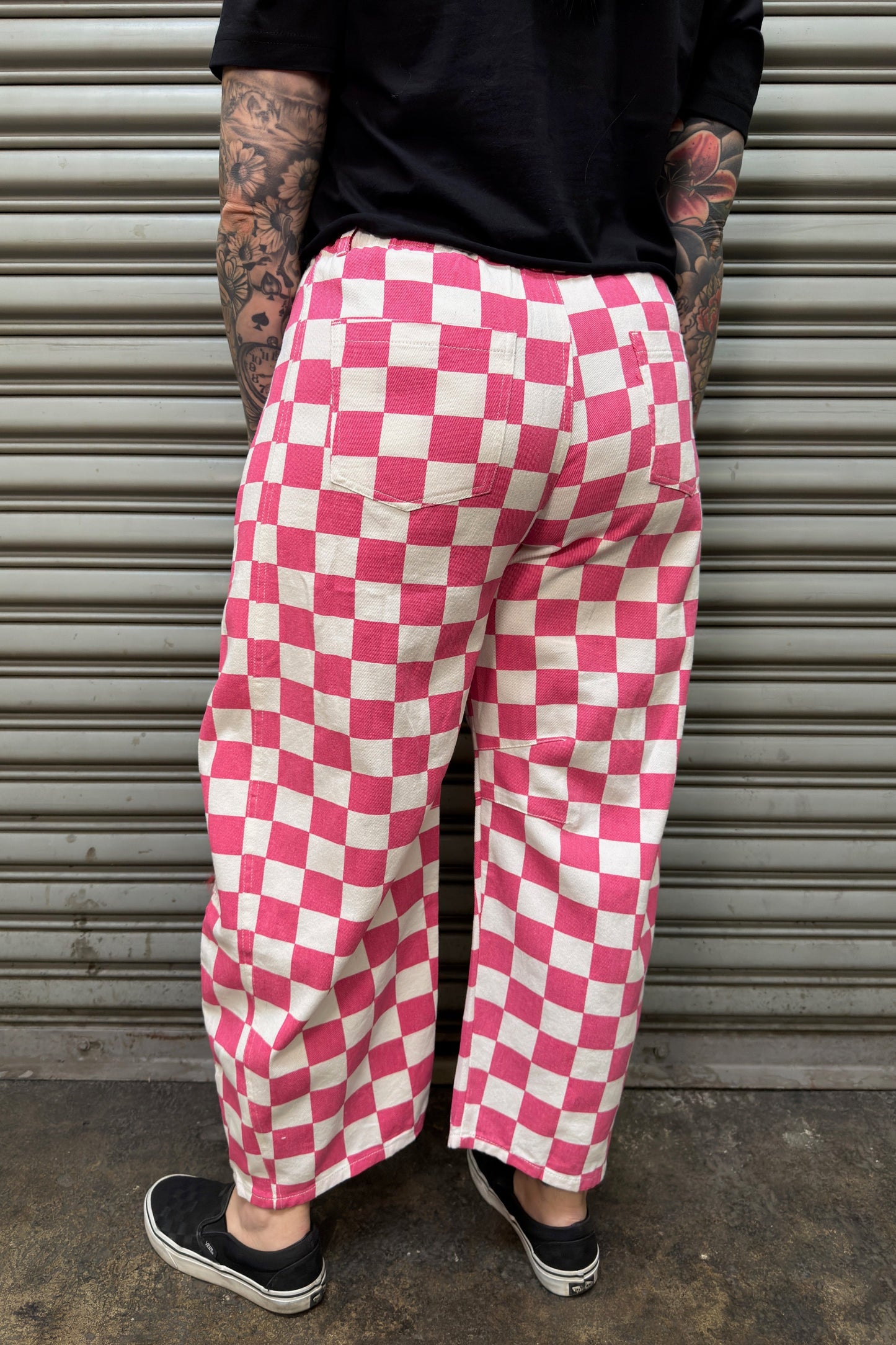 Person wearing pink and white checkered pants standing in front of a metal shutter.
