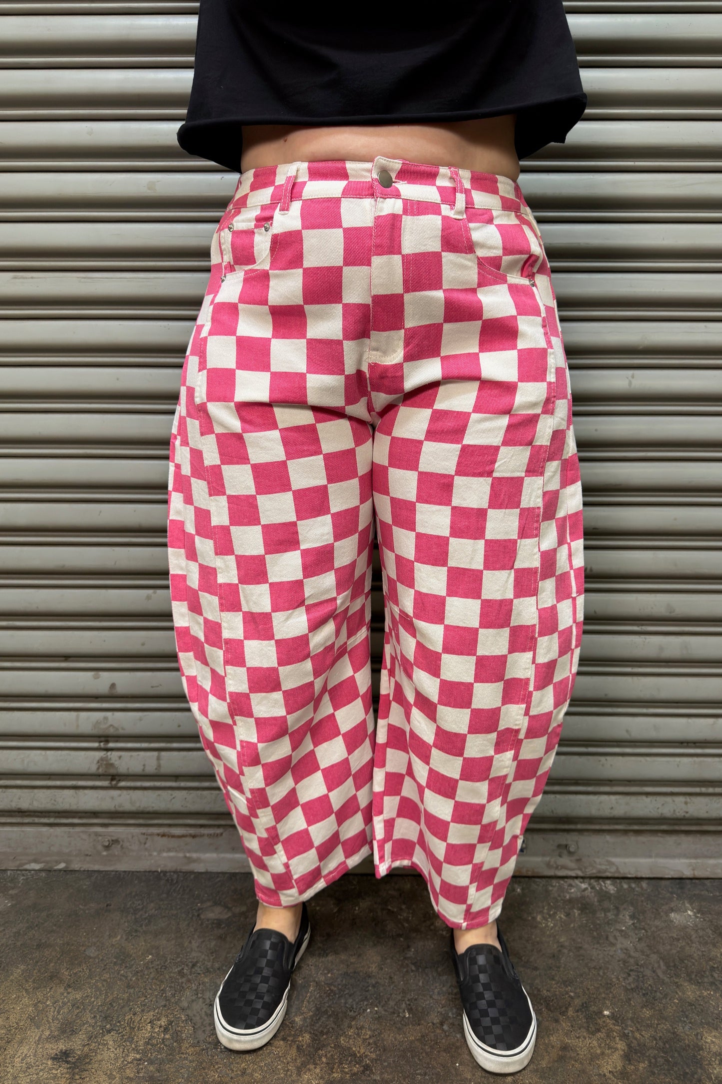Person wearing pink and white checkered pants standing in front of a metal shutter.