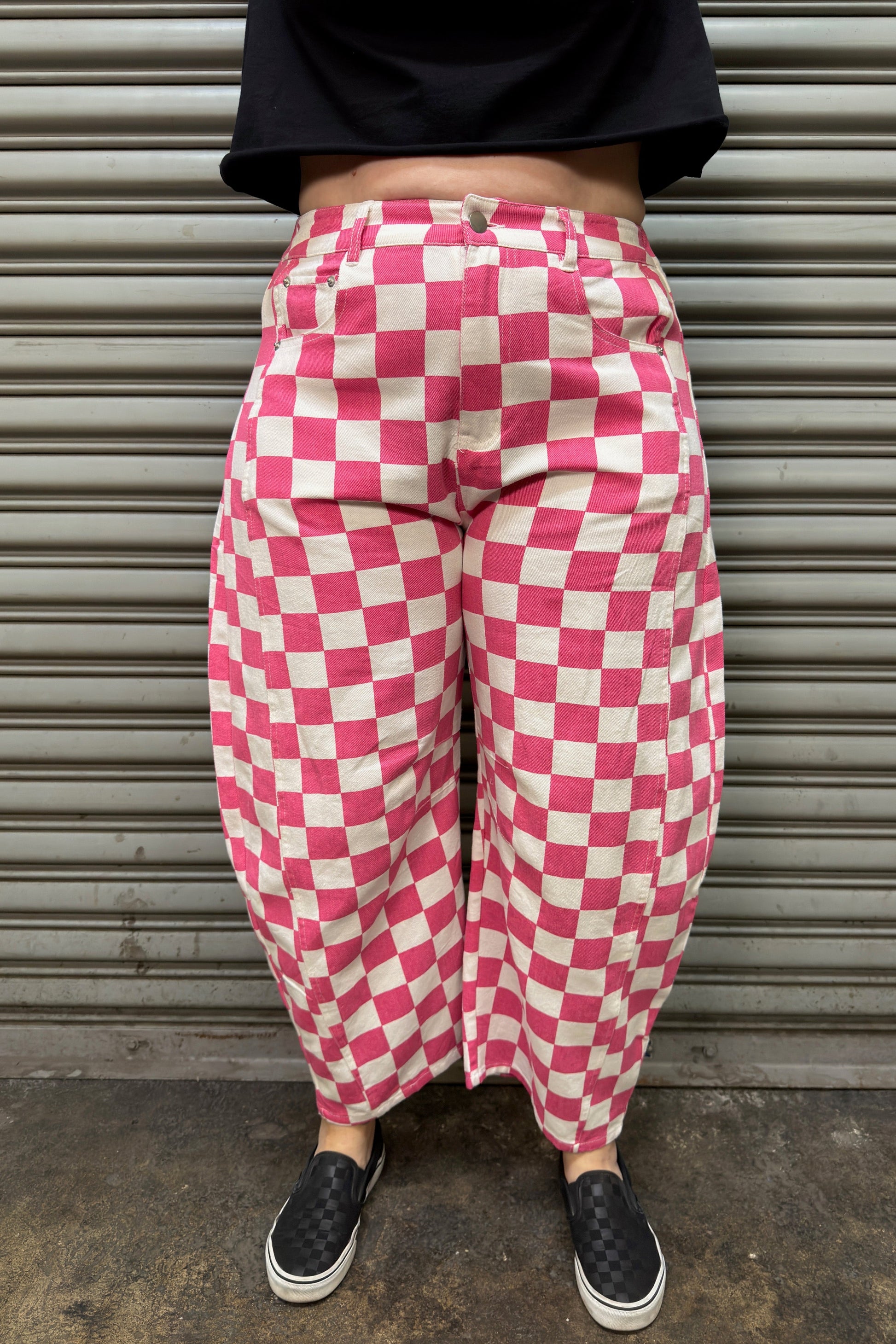 Person wearing pink and white checkered pants standing in front of a metal shutter.