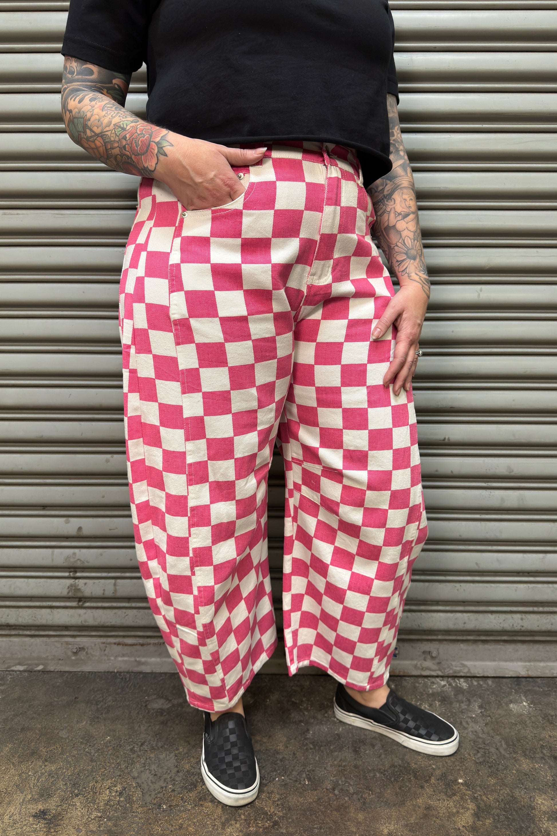 Person wearing pink and white checkered pants standing against a metal shutter.