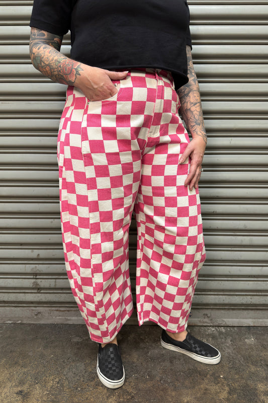 Person wearing pink and white checkered pants standing against a metal shutter.
