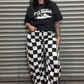Person wearing a black t-shirt and checkered pants standing in front of a metal shutter.