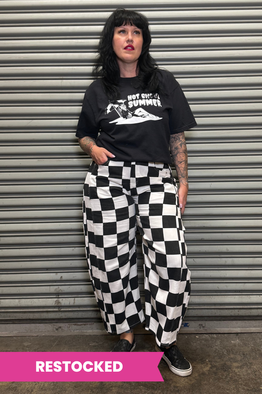 Person wearing a black t-shirt and checkered pants standing in front of a metal shutter.